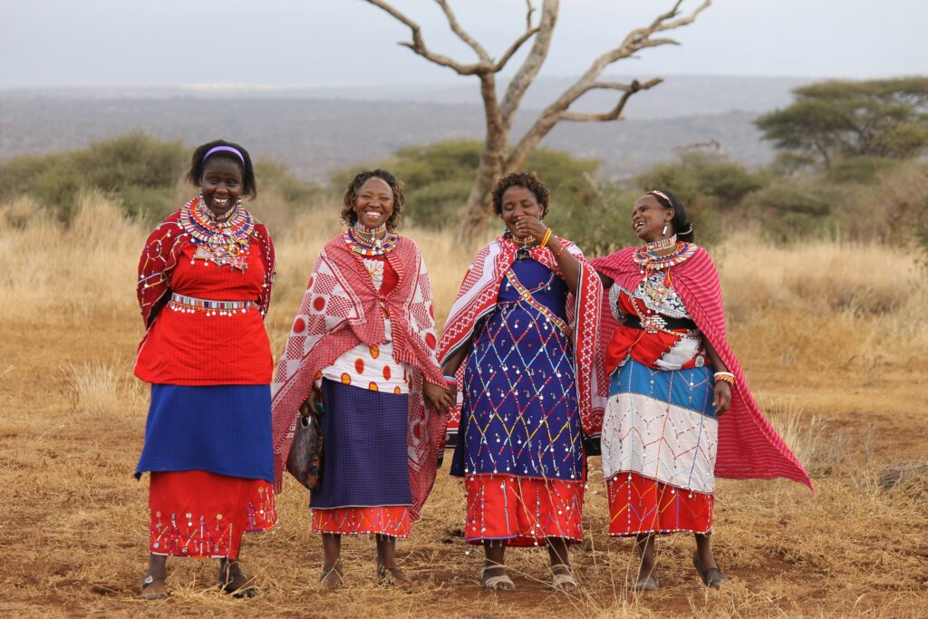 A group of Maasai women smile and pose for a photo wearing traditional attires